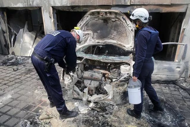 Police officers work on a charred car at the city hall of Mons-en-Barœul, northern France Thursday