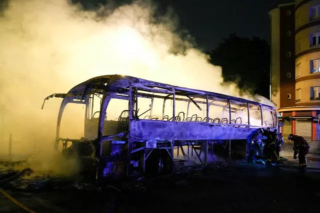 Firefighters use a water hose on a burnt bus in Nanterre near Paris
