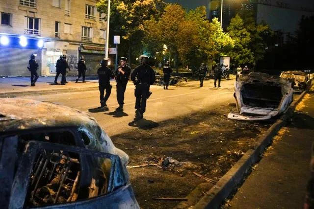 Police officers pass by charred cars in Nanterre