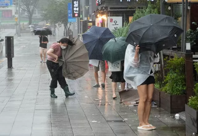 People struggle to hold onto their umbrellas in the rain and wind in Busan