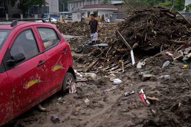 A man walks by a damaged vehicle in the aftermath of flood waters from an overflowing river in the Mentougou district on the outskirts of Beijing