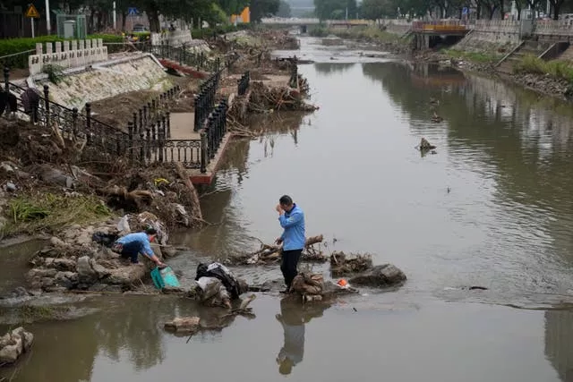 Residents on a damaged bank of a canal clogged with flood debris