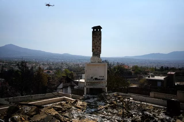 A helicopter flies near a burnt house in Acharnes suburb, on Mount Parnitha, in north-western Athens, Greece