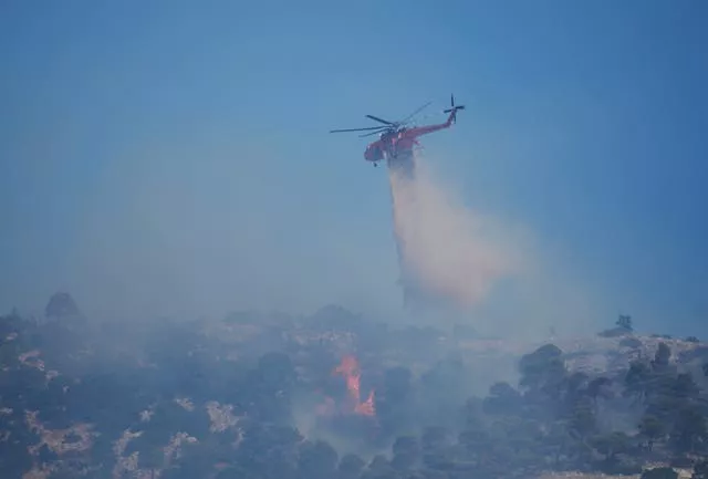 A helicopter drops water over a wildfire atop Mount Parnitha, in north-western Athens, Greece