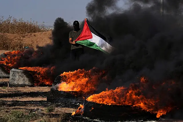 A masked Palestinian protester waves his national flag next to burning tyres during clashes with Israeli security forces