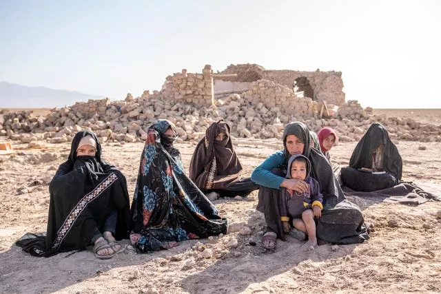 Mulheres afegãs sentam-se em frente a casas que foram destruídas