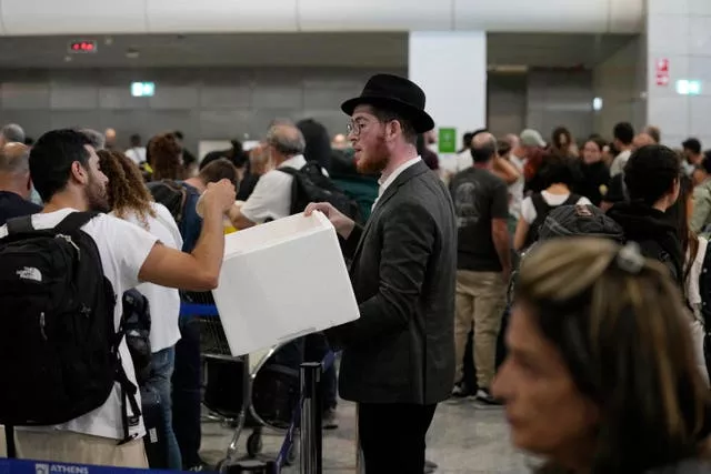 A man distributes sandwiches to passengers who are waiting in a queue to board flights to Israel at the Eleftherios Venizelos International Airport in Athens, Greece