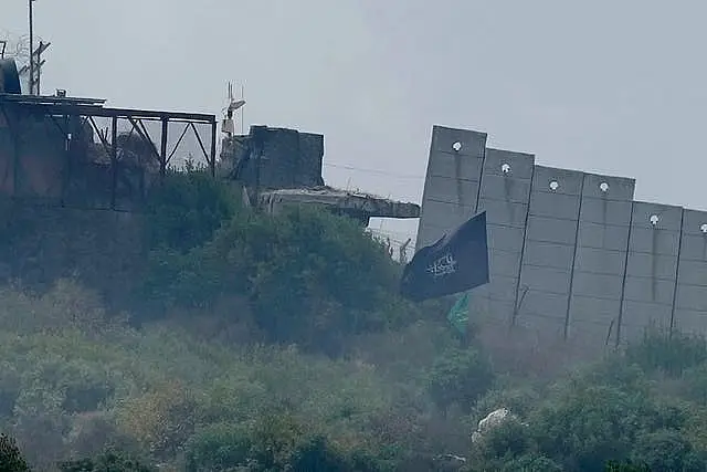 A black religious flag, right, with Arabic words reading 'Oh Hussein', planted by Hezbollah fighters is seen on the fence of an Israeli army position