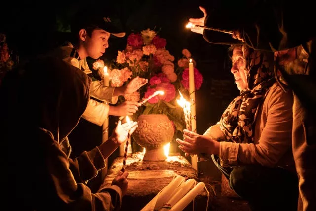People hold candles over a tomb decorated with flowers at a cemetery in Atzompa