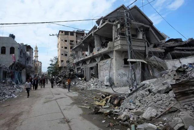 Palestinos passam por edifícios destruídos no bombardeio israelense na Faixa de Gaza, na estrada principal do campo de refugiados de Bureij, Faixa de Gaza 