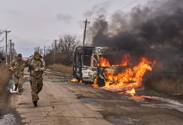 Ukrainian soldiers pass by a burning volunteer bus