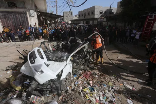 Palestinians stand around a car targeted in an Israeli air strike in Rafah