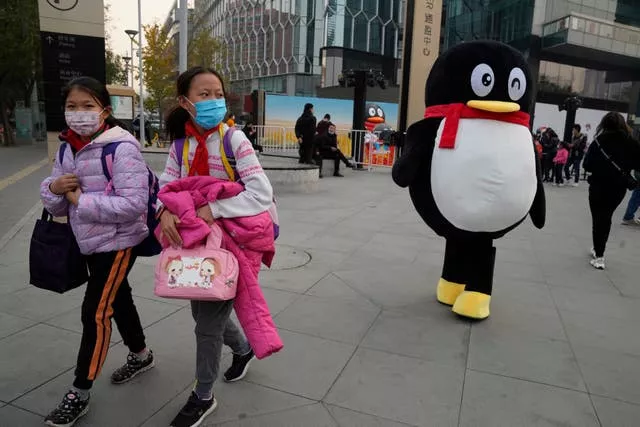Children pass a mascot for Tencent during a promotional event in Beijing