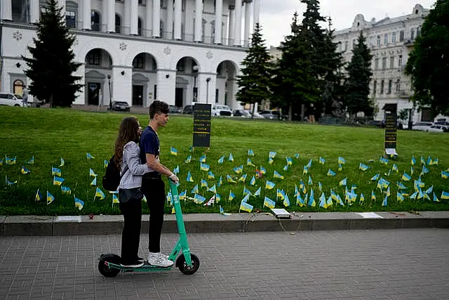 A couple ride a scooter in front of flags honouring soldiers killed fighting Russian troops in Independence Square in Kyiv, Ukraine