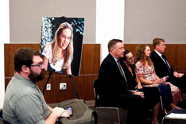 Chris Lambert, documentary podcaster, sits in front of a poster of Kristin Smart with family members nearby hours after a jury found Paul Flores guilty of the 1996 murder of Cal Poly student Kristin Smart 