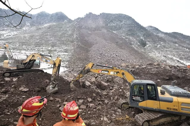 Equipes de resgate observam escavadeiras cavando no local de um deslizamento de terra na vila de Liangshui 