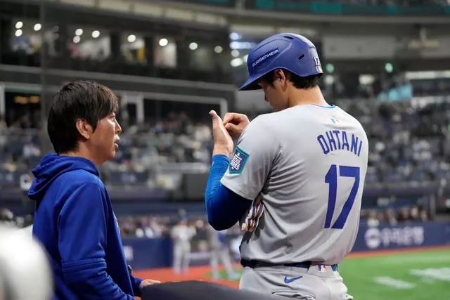 O rebatedor designado do Los Angeles Dodgers, Shohei Ohtani, à direita, fala com seu intérprete Ippei Mizuhara durante o quinto turno de um jogo de beisebol do dia de abertura contra o San Diego Padres no Gocheok Sky Dome em Seul, Coreia do Sul, em 20 de março