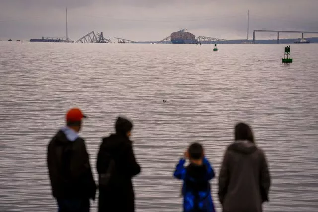 People at Fort Mchenry view a container ship as it rests against the wreckage of the Francis Scott Key Bridge in Baltimore