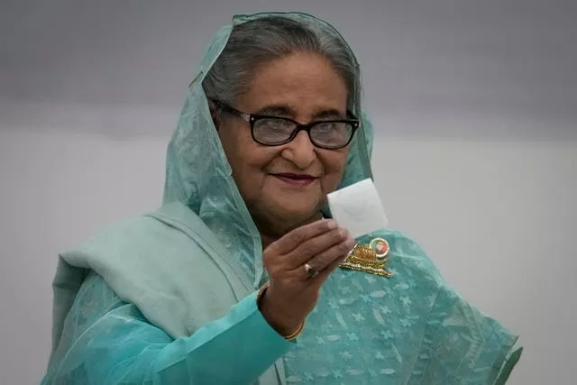 Head and shoulders image of Sheikh Hasina, smiling and holding up a piece of paper