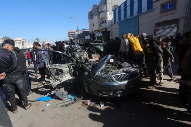 Palestinians look at a car targeted by an Israeli air strike in Rafah, Gaza Strip