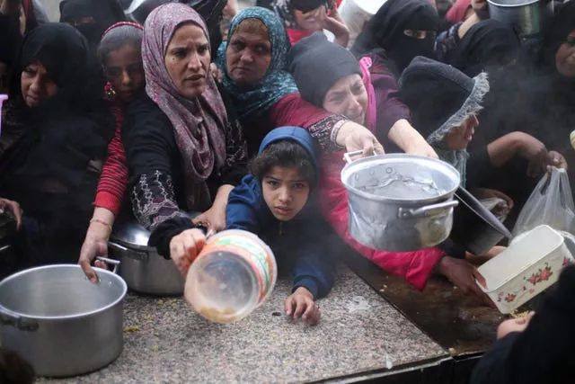 Palestinos fazem fila para distribuição gratuita de alimentos durante a ofensiva aérea e terrestre israelense em Khan Younis, Faixa de Gaza