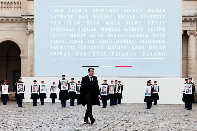 French President Emmanuel Macron walks past French Republican Guards who hold portraits of the French victims of the October 7 2023 Hamas attack, during a ceremony at the Invalides monument