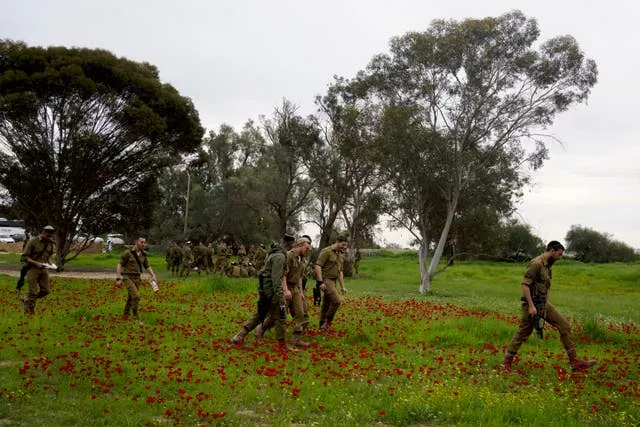 Soldados israelenses caminham por um tapete de flores silvestres de anêmona vermelha em flor em Re'im, sul de Israel, no local de um ataque transfronteiriço do Hamas durante o festival de música Nova, onde centenas de foliões foram mortos e sequestrados na Faixa de Gaza (Maya Alleruzzo/AP)