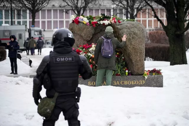 Un policier regarde un homme déposer des fleurs pour rendre un dernier hommage à Alexei Navalny au mémorial où le premier camp du système carcéral politique du Goulag a été établi, à Saint-Pétersbourg, en Russie.