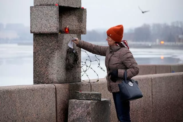 A woman places a piece of paper with words of grief for Alexei Navalny  at the Memorial to Victims of Political Repression in St Petersburg, Russia