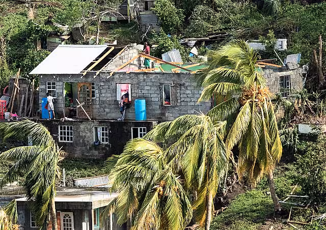 A damaged house, missing part of its roof, surrounded by trees