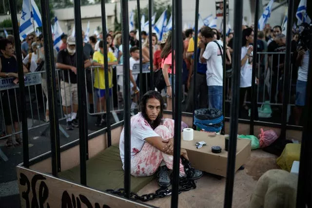 Une femme assise dans une cage lors d'une manifestation marquant le neuf mois du début de la guerre et exigeant la libération des otages