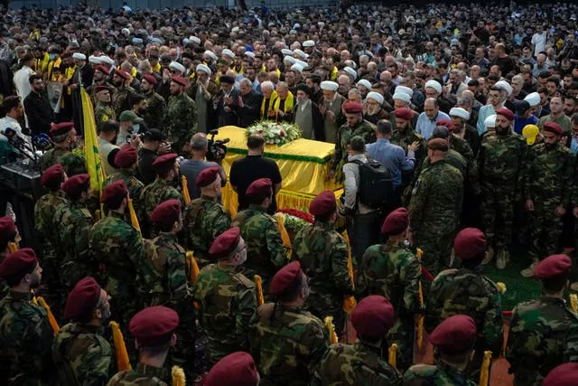Soldiers stand to attention and look on at coffin draped in yellow 