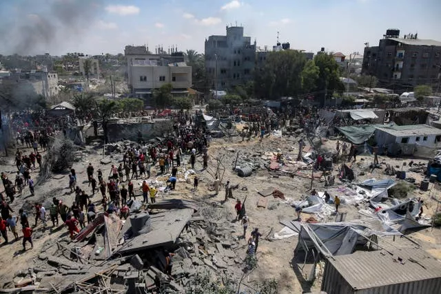 A bomb crater surrounded by damaged buildings and people