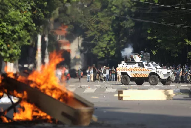 Police firing tear gas shells and rubber bullets at protesting students in Dhaka, Bangladesh, as a fire burns in the foreground