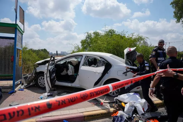 Police strand by a damaged white car near a bus stop