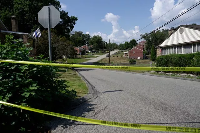 Police tape is strung across a road with a house in the background