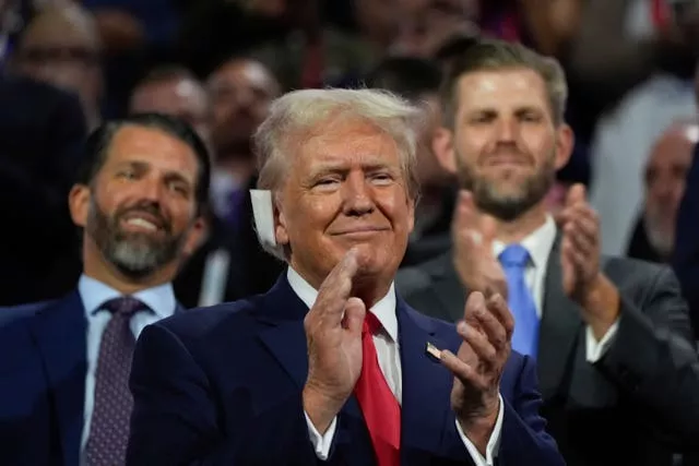 Donald Trump with a bandage on his right ear applauding while his two sons stand behind him