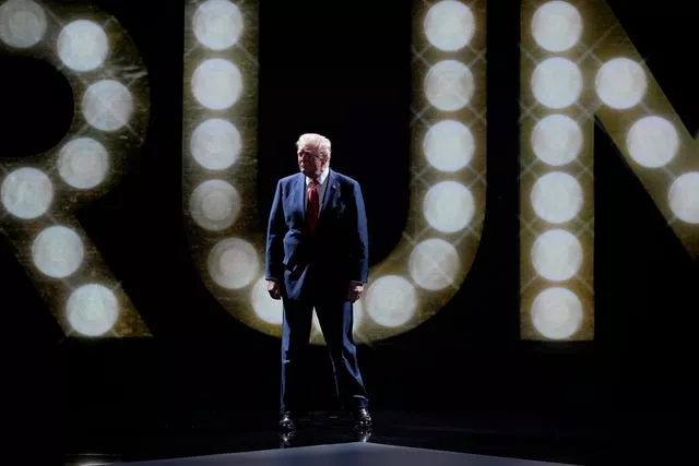 Donald Trump stands in front of 'Trump' in lights