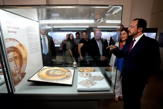 President Nikos Christodoulides stands in front of an Orthodox Christian icon in a glass case