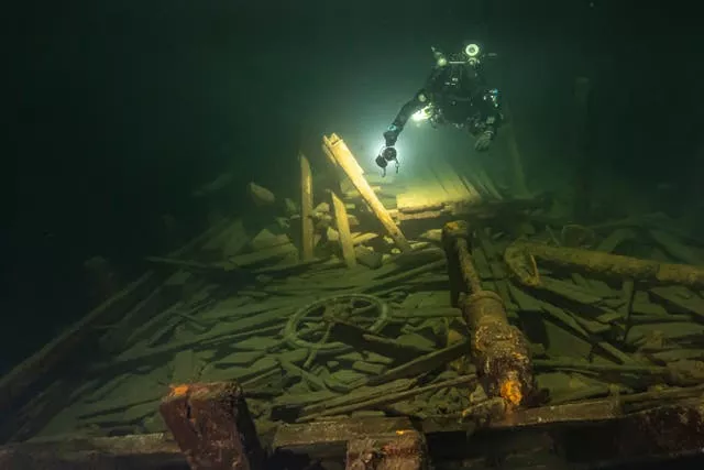 The shipwreck illuminated by a diver's torch in dark water