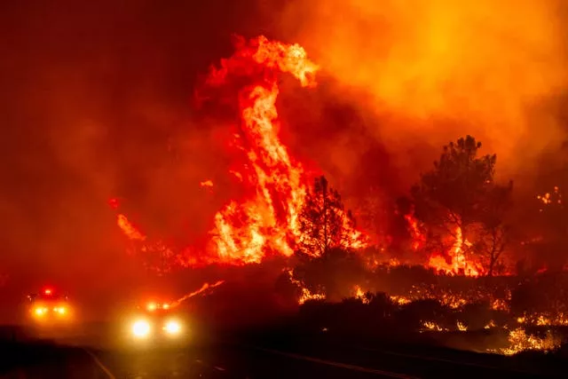 Flames leap above fire vehicles driving along a road in Tehama County, California