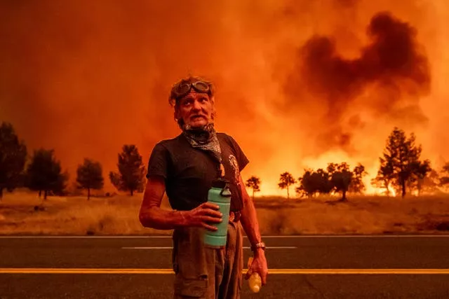 A man stands in front of a blazing fire 