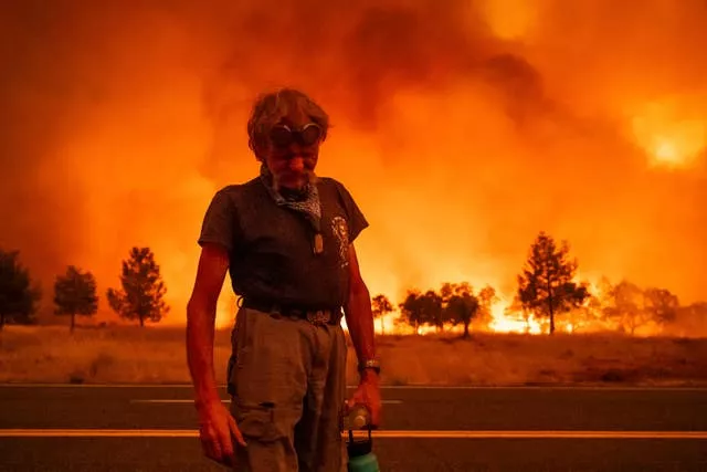 A man pauses while evacuating from an area where a wildfire is seen burning trees