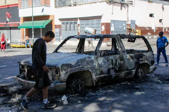 Residents stand around a vehicle burned during the previous day’s protests against official election results 