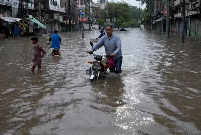 Motorcyclists riding through a flooded road caused by heavy monsoon rainfall in Lahore, Pakistan