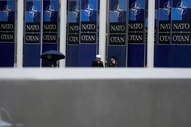 Two military personnel walk by Nato banners prior to a wreath-laying ceremony at Nato headquarters in Brussels 