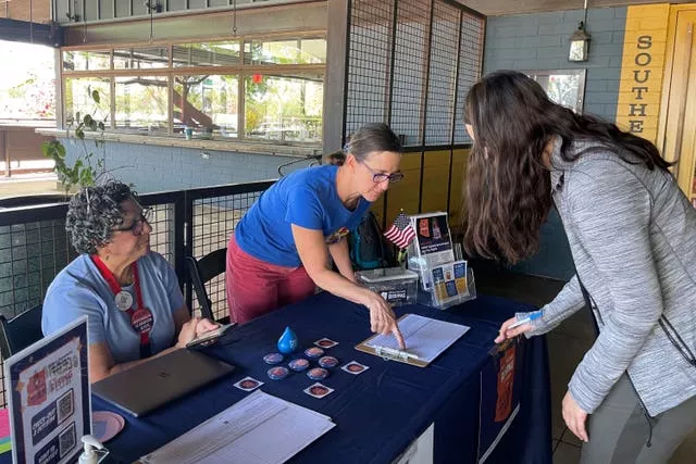 Volunteer signature gatherers watch as voter Grace Harders prepares to sign a petition that aims to enshrine the right to abortion in Arizona 
