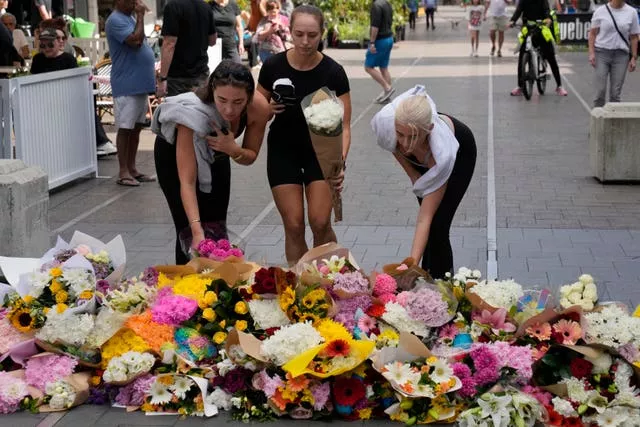 Three women place flowers as a tribute near the crime scene at Bondi Junction in Sydney