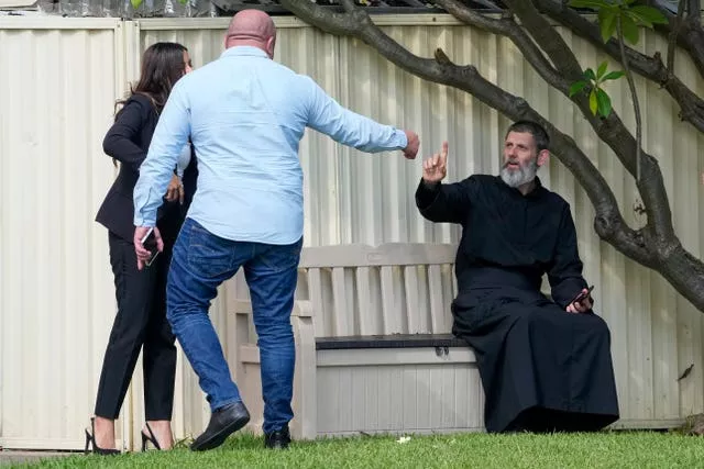 Father Daniel Kochou, right, gestures as he speaks with people across the road from the Christ the Good Shepherd church
