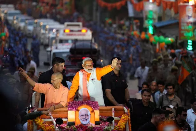 Indian Prime Minister Narendra Modi, in a white waistcoat, and Yogi Adityanath, chief minister of Uttar Pradesh, greet supporters from a vehicle during a roadshow in Varanasi
